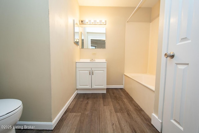 bathroom with baseboards, toilet, wood finished floors, a bathtub, and vanity