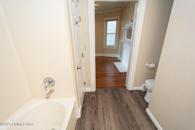 bathroom with baseboards, toilet, a tub, ornamental molding, and wood finished floors