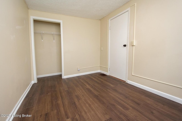 unfurnished bedroom featuring dark wood-type flooring, a closet, a textured ceiling, and baseboards