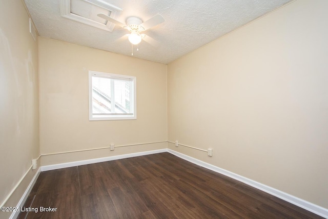 empty room with attic access, dark wood-style flooring, a textured ceiling, and baseboards