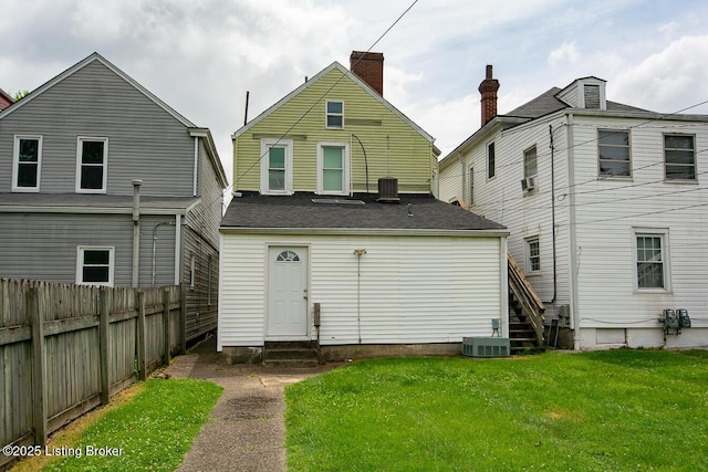 back of property with entry steps, a yard, central AC, and fence