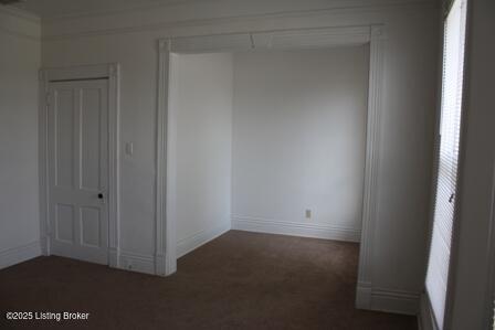 unfurnished room featuring dark carpet and baseboards