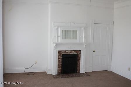 unfurnished living room featuring crown molding, dark colored carpet, a fireplace, and baseboards