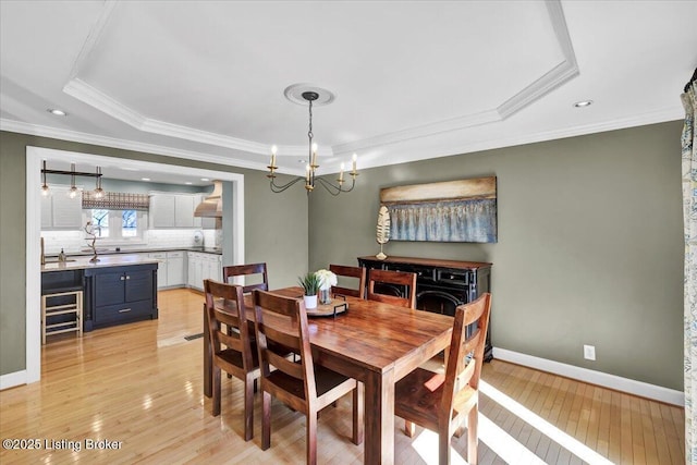 dining area with a notable chandelier, baseboards, ornamental molding, light wood finished floors, and a raised ceiling