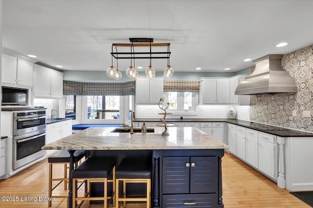 kitchen featuring tasteful backsplash, custom range hood, black appliances, white cabinetry, and a sink