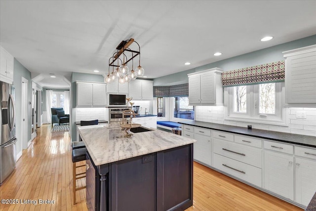 kitchen featuring a kitchen island with sink, white cabinetry, light wood-style floors, appliances with stainless steel finishes, and decorative backsplash