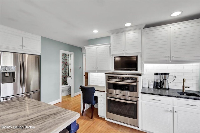 kitchen with stainless steel appliances, tasteful backsplash, white cabinets, a sink, and light wood-type flooring