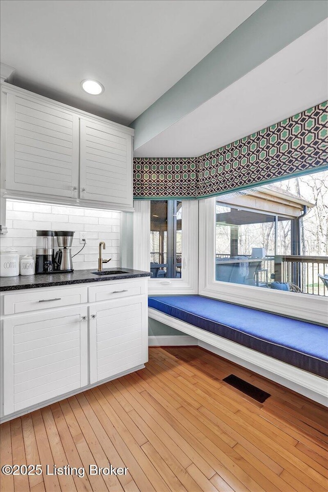 kitchen featuring a sink, visible vents, light wood-type flooring, tasteful backsplash, and dark countertops