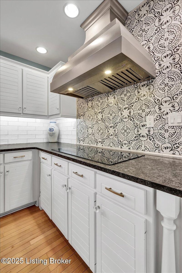 kitchen with black electric stovetop, extractor fan, light wood-style flooring, white cabinetry, and tasteful backsplash