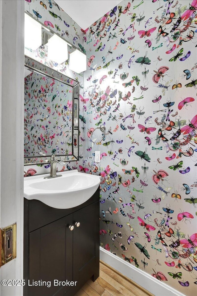 bathroom with baseboards, wood finished floors, vanity, and wallpapered walls