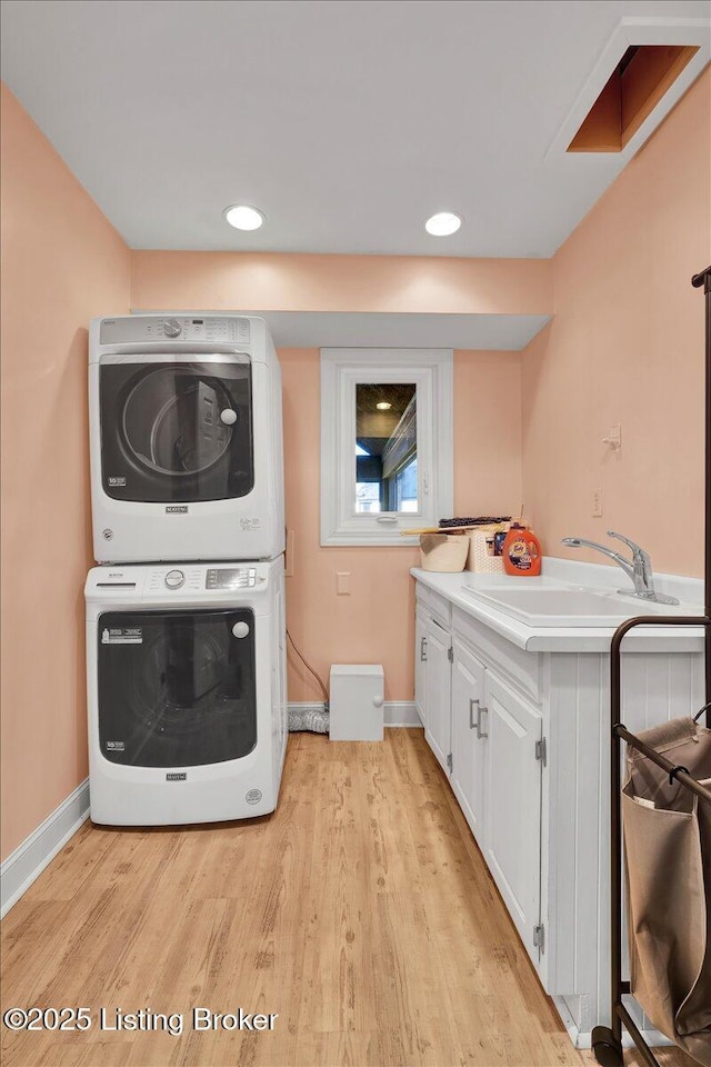 laundry area featuring light wood finished floors, cabinet space, baseboards, stacked washer and clothes dryer, and a sink