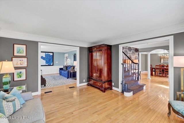 living room featuring arched walkways, light wood-style floors, stairs, ornamental molding, and decorative columns