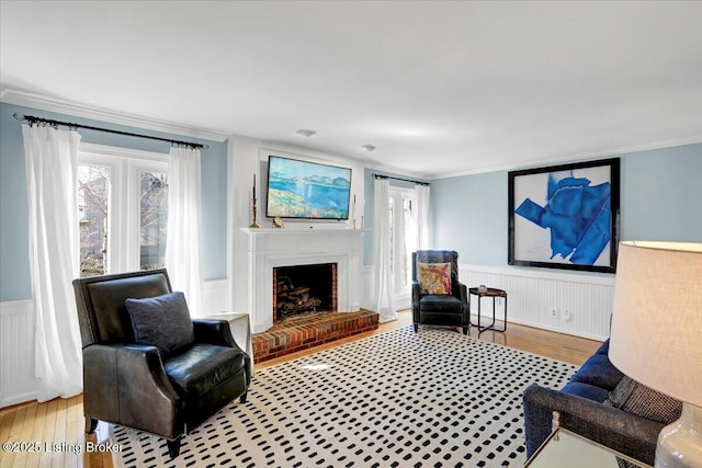 living area with a wainscoted wall, plenty of natural light, ornamental molding, and hardwood / wood-style floors