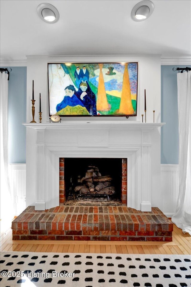 details featuring a brick fireplace, a wainscoted wall, crown molding, and wood finished floors