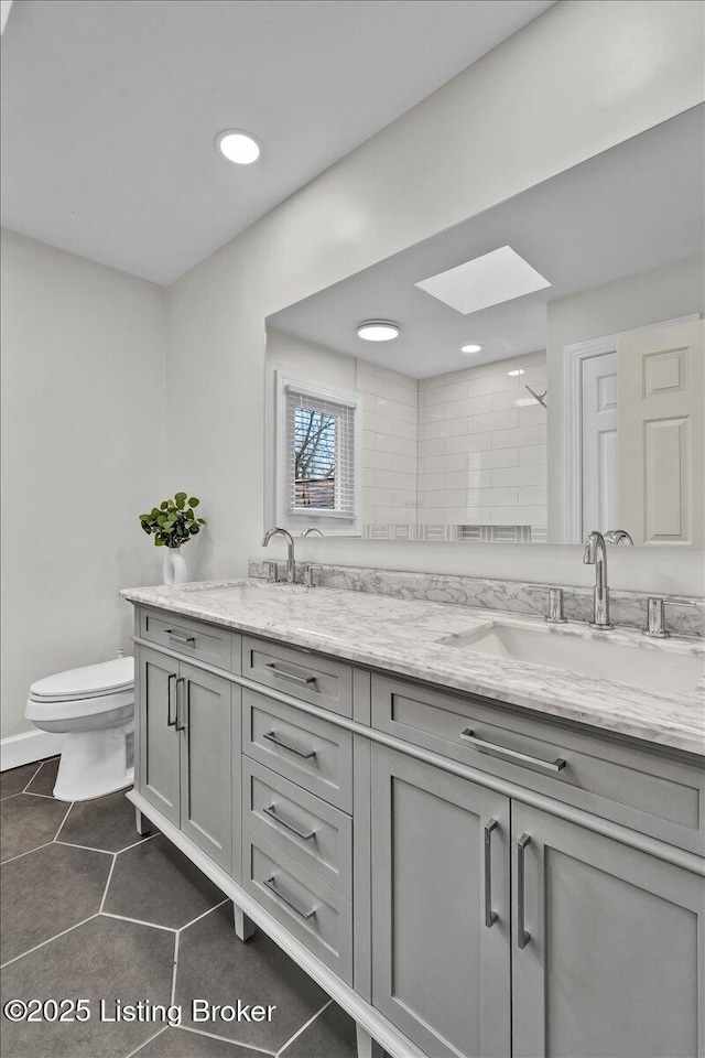 full bath with double vanity, a skylight, toilet, and a sink