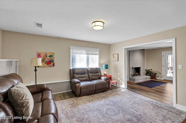 living area with visible vents, a fireplace, baseboards, and wood finished floors