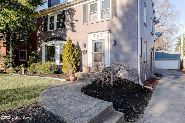 view of front of house featuring a garage, a chimney, an outbuilding, a front lawn, and brick siding