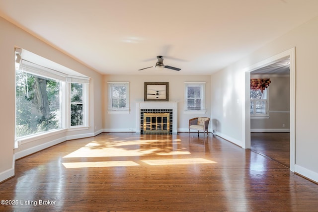 unfurnished living room featuring ceiling fan, a fireplace, baseboards, and wood finished floors