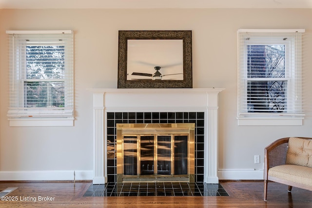 details featuring baseboards, a tiled fireplace, and wood finished floors