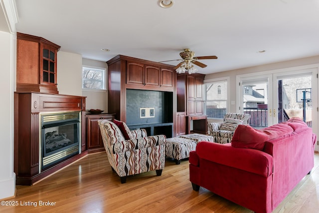 living room featuring recessed lighting, light wood-style flooring, a ceiling fan, and a glass covered fireplace