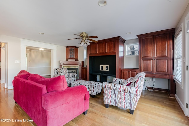 living area with ceiling fan, a fireplace, light wood-style flooring, and baseboards