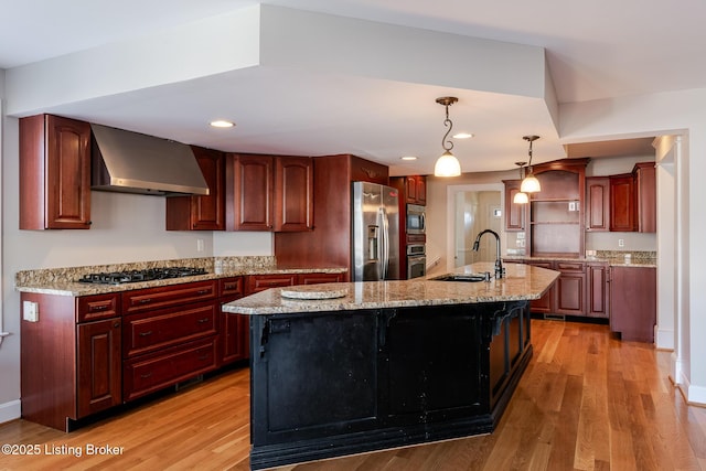 kitchen featuring stainless steel appliances, a kitchen island with sink, a sink, and wall chimney exhaust hood