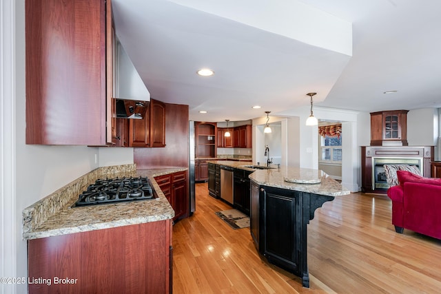 kitchen featuring hanging light fixtures, a sink, a kitchen island with sink, and light stone countertops