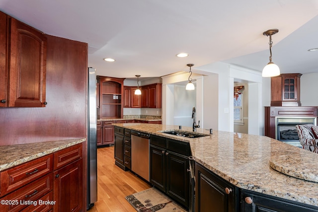 kitchen with a sink, appliances with stainless steel finishes, light stone counters, and decorative light fixtures