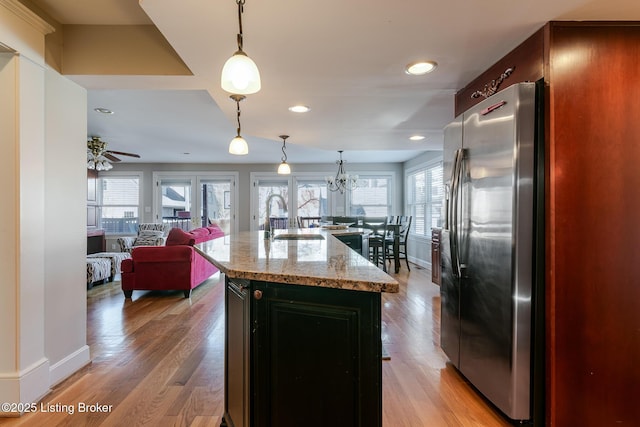 kitchen featuring an island with sink, hanging light fixtures, light stone countertops, stainless steel refrigerator with ice dispenser, and a sink