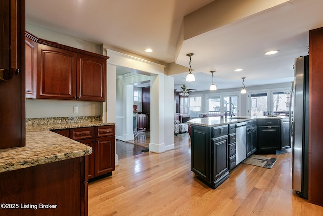 kitchen with light stone counters, decorative light fixtures, stainless steel appliances, a sink, and a peninsula