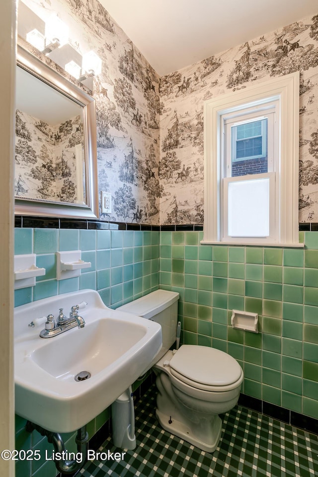 half bath featuring toilet, wallpapered walls, and wainscoting