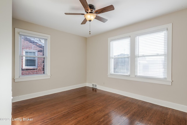 unfurnished room with dark wood-style floors, visible vents, baseboards, and a ceiling fan