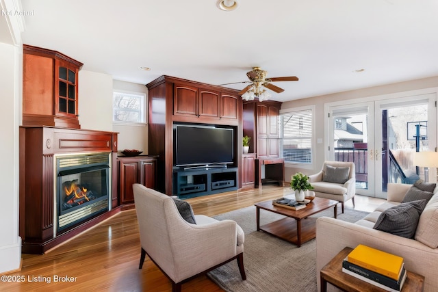 living room featuring a ceiling fan, a glass covered fireplace, wood finished floors, french doors, and recessed lighting