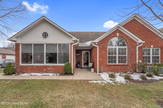 view of front of house featuring a sunroom, a front lawn, and brick siding