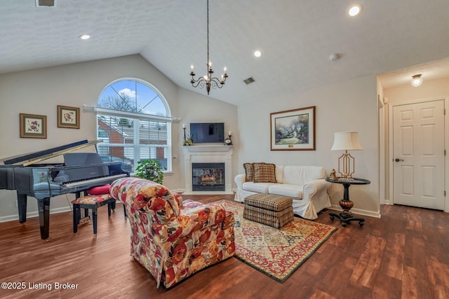 living area featuring visible vents, vaulted ceiling, wood finished floors, and a glass covered fireplace