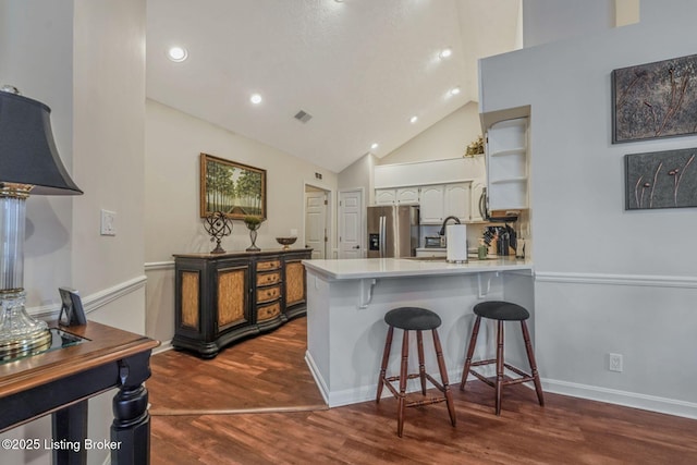 kitchen with stainless steel fridge, visible vents, dark wood-type flooring, a peninsula, and a kitchen bar