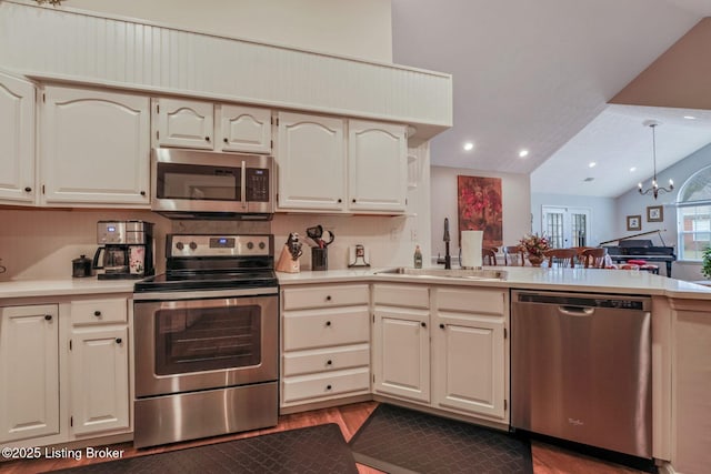 kitchen with a peninsula, a sink, vaulted ceiling, light countertops, and appliances with stainless steel finishes