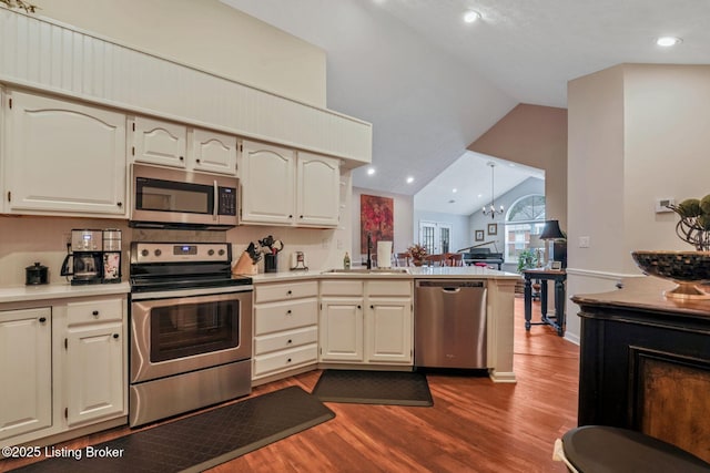 kitchen with dark wood finished floors, lofted ceiling, appliances with stainless steel finishes, a peninsula, and a sink