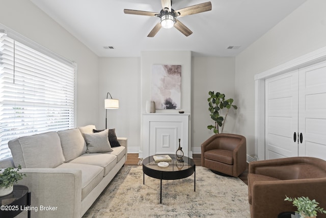 living room with light wood-type flooring, visible vents, ceiling fan, and baseboards