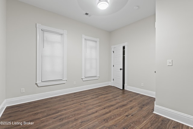 empty room with dark wood-style floors, baseboards, and visible vents