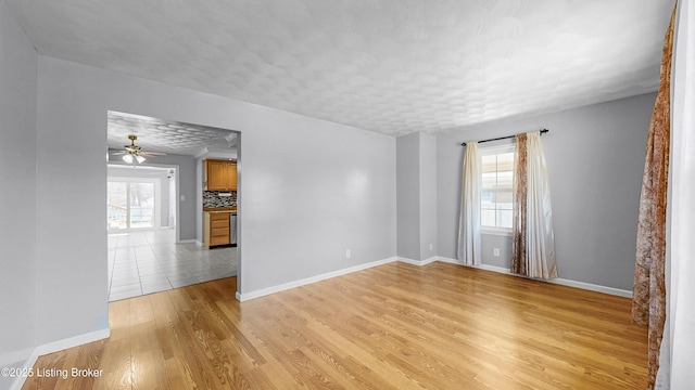 unfurnished room with a ceiling fan, light wood-style flooring, baseboards, and a textured ceiling