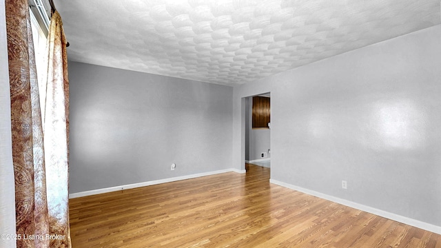 empty room featuring light wood-type flooring, baseboards, and a textured ceiling