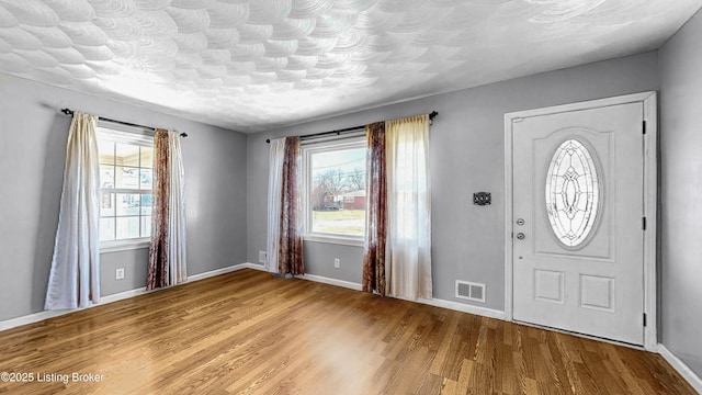 foyer featuring baseboards, a textured ceiling, visible vents, and wood finished floors