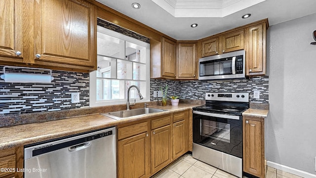 kitchen featuring tasteful backsplash, brown cabinets, stainless steel appliances, a sink, and light tile patterned flooring