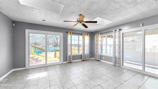 tiled empty room with a skylight, ceiling fan, baseboards, and a textured ceiling