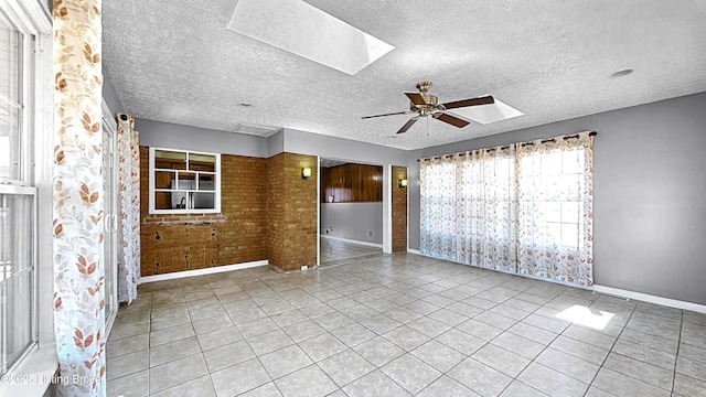 tiled spare room with ceiling fan, a textured ceiling, and a skylight