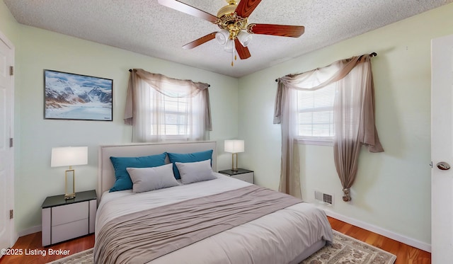 bedroom featuring multiple windows, visible vents, a textured ceiling, and wood finished floors