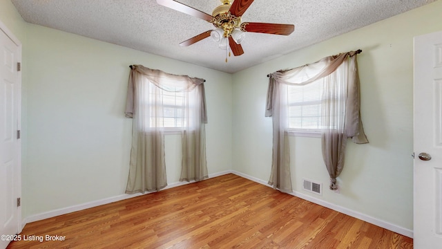 spare room featuring light wood-style floors, a healthy amount of sunlight, visible vents, and a textured ceiling