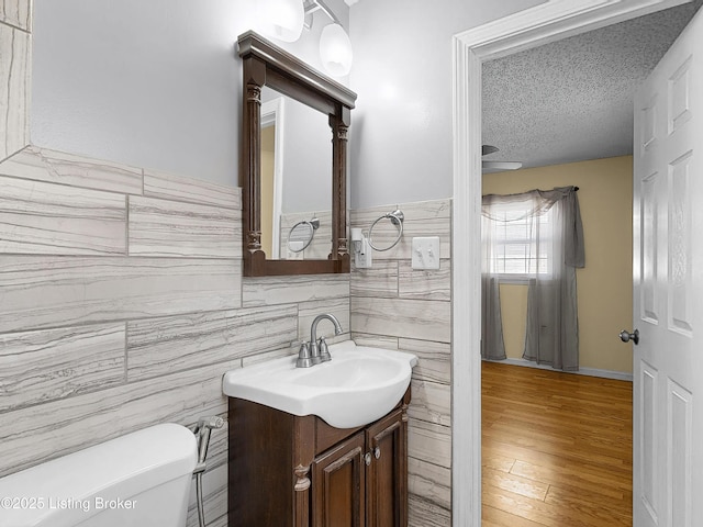 half bathroom featuring toilet, wood finished floors, a textured ceiling, vanity, and tile walls