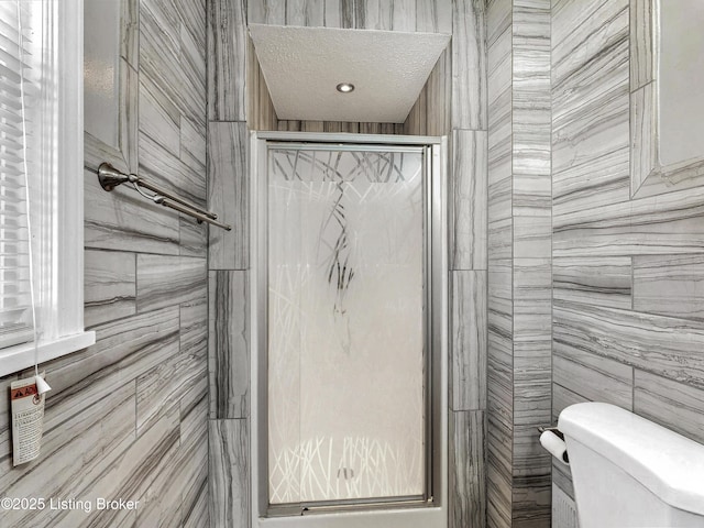 bathroom with a textured ceiling, a stall shower, toilet, and tile walls